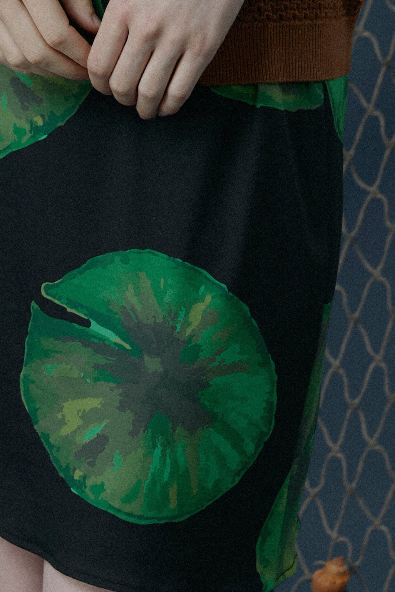 Close up of black knit jersey dress with hand drawn green lily pads on black background
